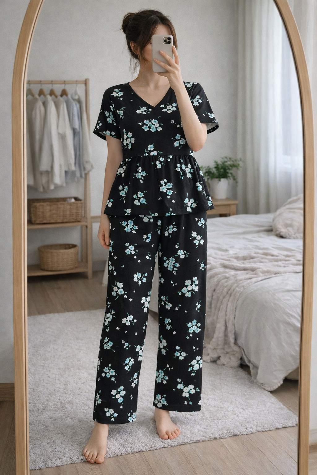 Woman wearing Blush Whispers black floral print peplum night suit with full-length pants, taking a mirror selfie in a cozy bedroom.