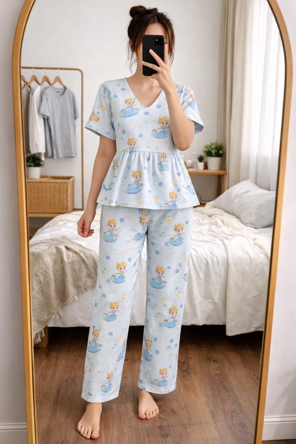 Woman wearing Blush Whispers blue peplum night suit with princess prints and subtle stripes, taking a mirror selfie in a cozy bedroom