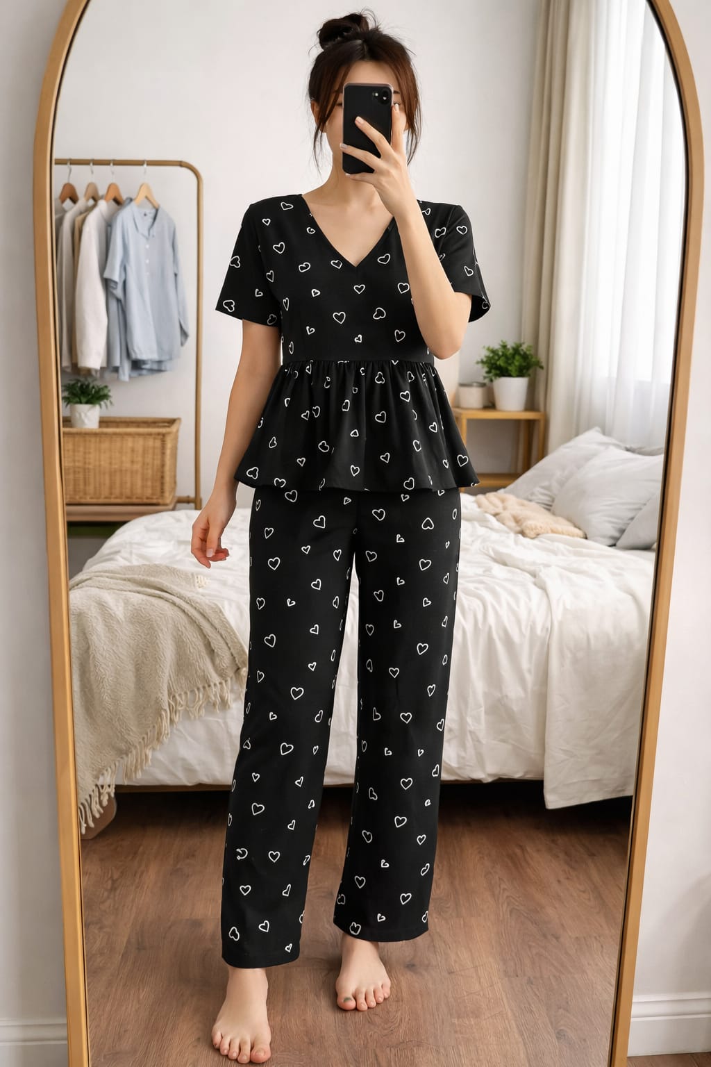 Woman wearing Blush Whispers black peplum night suit with white heart prints and full-length pants, taking a mirror selfie in a cozy bedroom.