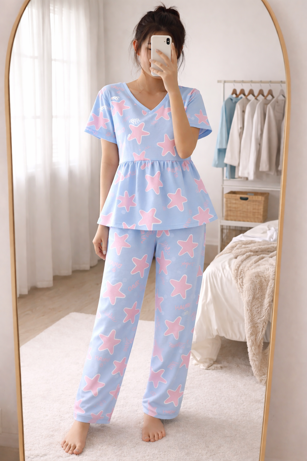 Woman wearing Blush Whispers sky blue peplum night suit with pink star prints and full-length pants, taking a mirror selfie in a cozy bedroom.