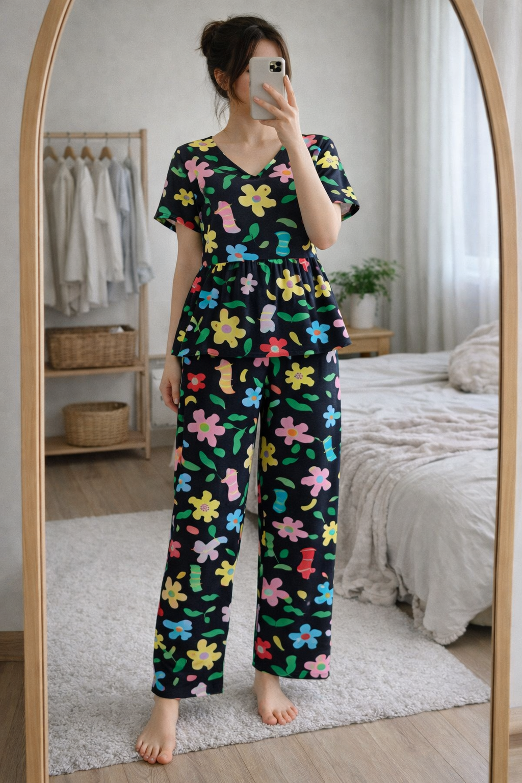 Woman wearing Blush Whispers black multicolor floral print peplum night suit with full-length pants, taking a mirror selfie in a cozy bedroom.