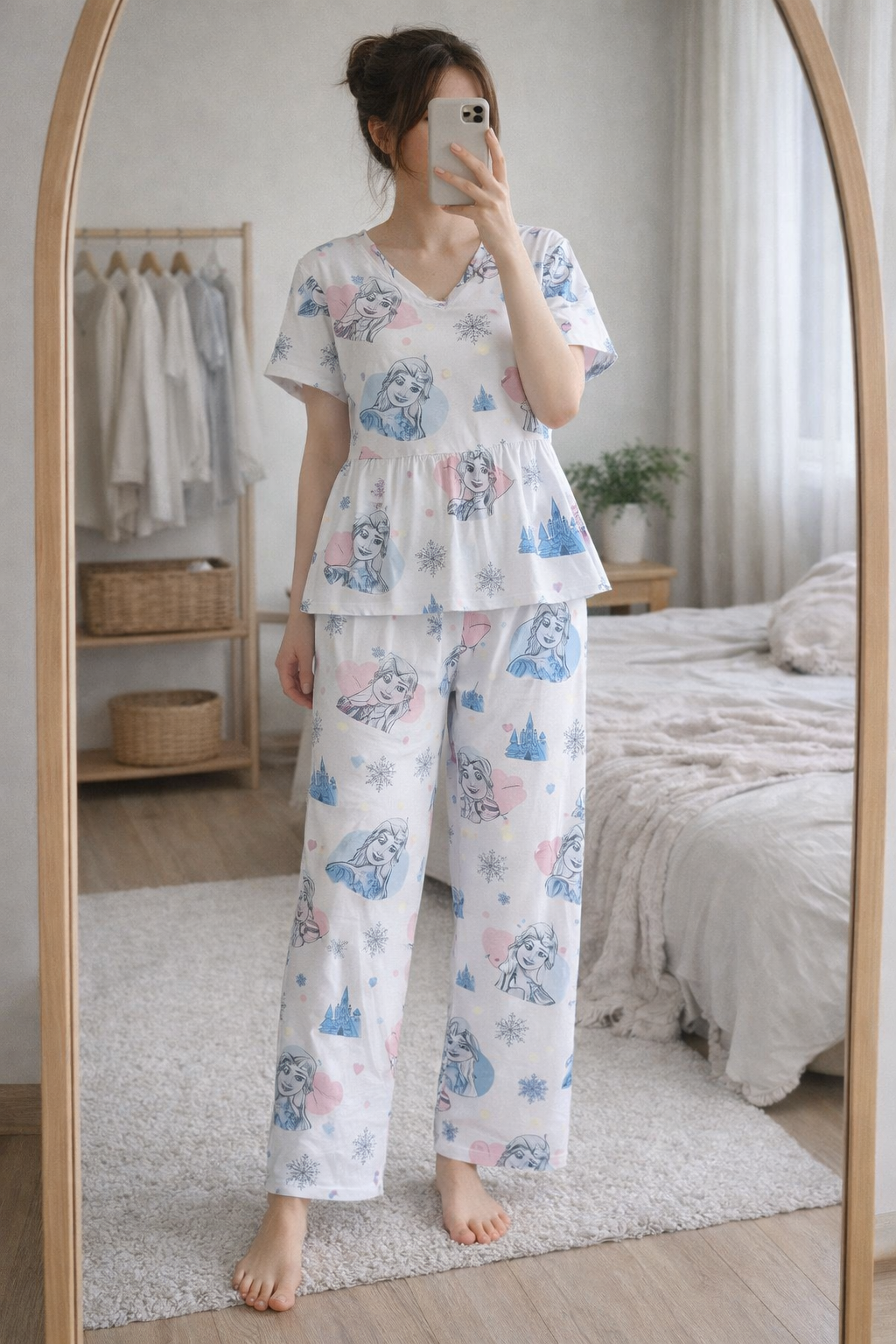 Woman wearing Blush Whispers white peplum night suit with princess and pastel prints, taking a mirror selfie in a cozy bedroom.