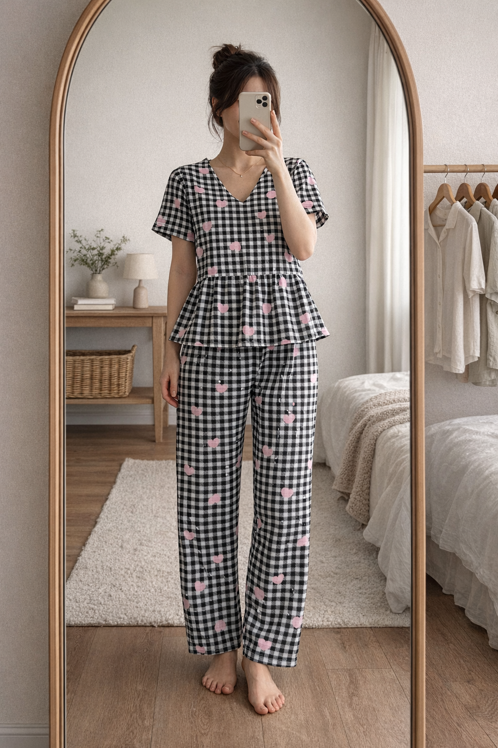 Woman wearing Blush Whispers black checkered peplum night suit with pink heart prints and full-length pants, taking a mirror selfie indoors.